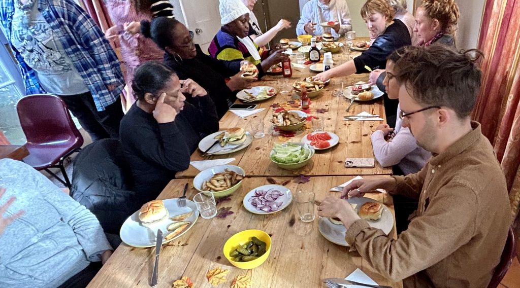 Photo of group of about 10 people sitting around a table sharing lunch family style and chatting